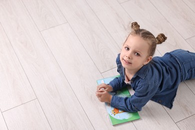 Cute little girl with book on warm floor at home, space for text. Heating system