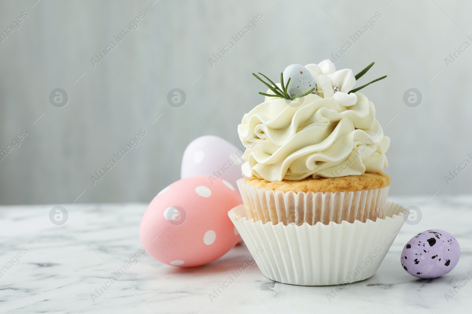 Photo of Tasty Easter cupcake with vanilla cream and eggs on white marble table, space for text