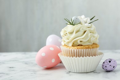 Tasty Easter cupcake with vanilla cream and eggs on white marble table, space for text