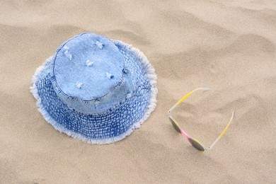 Photo of Jeans hat and sunglasses on sand, above view. Beach accessories