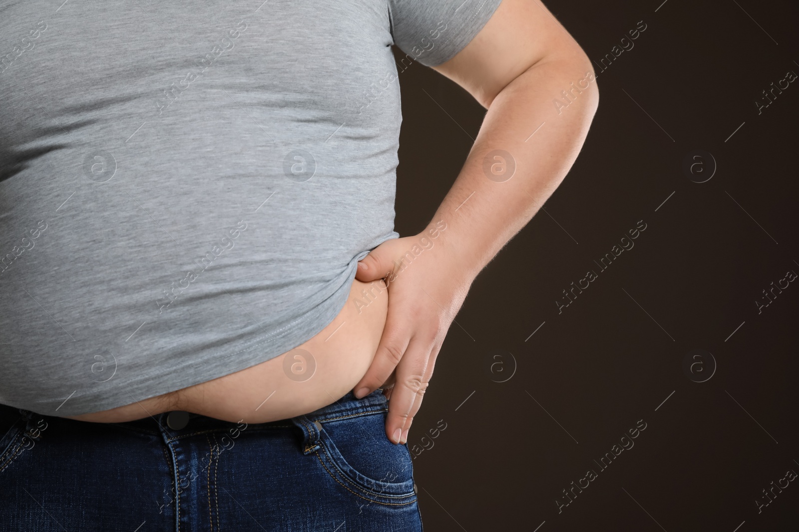 Photo of Overweight man in tight t-shirt on dark brown background, closeup. Space for text.