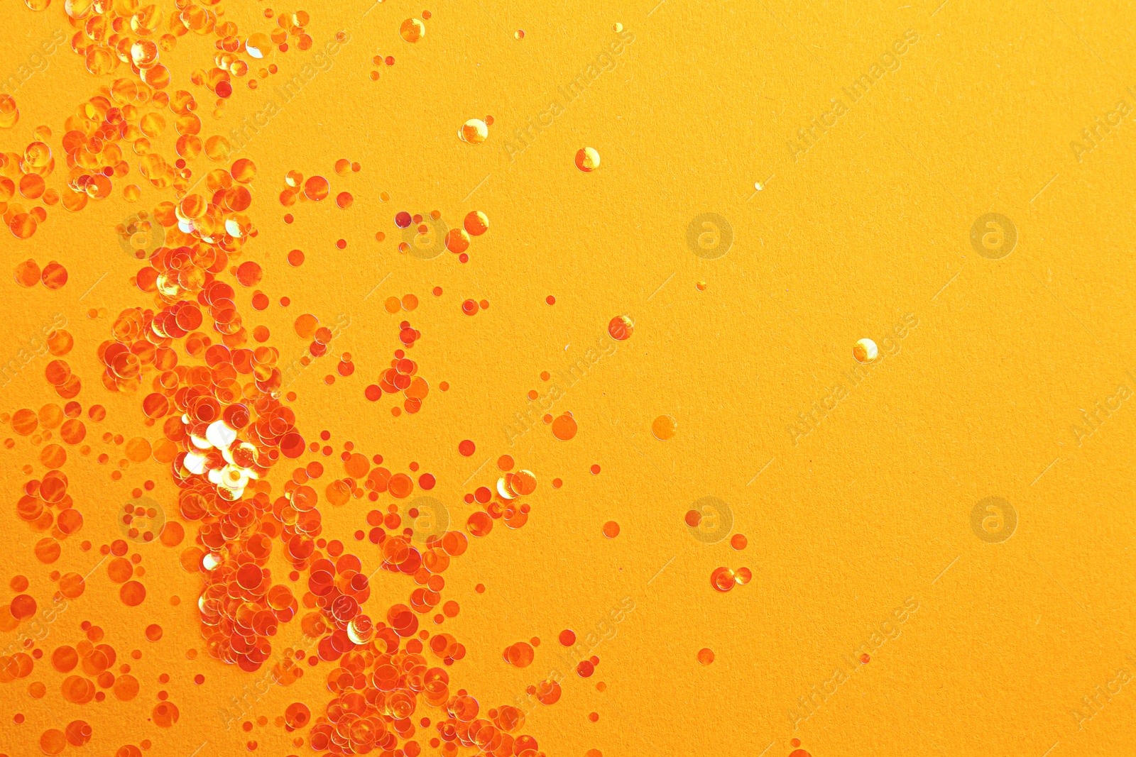 Photo of Shiny bright glitter on orange background, flat lay. Space for text