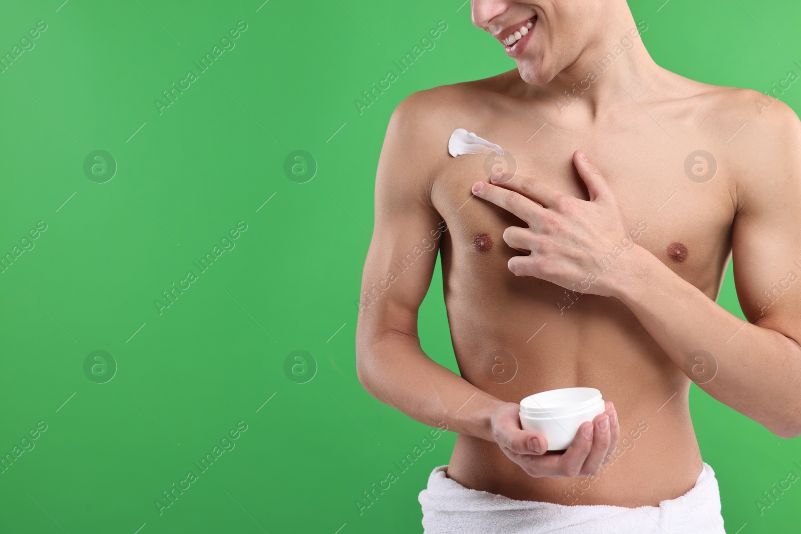 Photo of Man applying moisturizing cream onto his shoulder on green background, closeup. Space for text