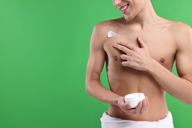 Man applying moisturizing cream onto his shoulder on green background, closeup. Space for text