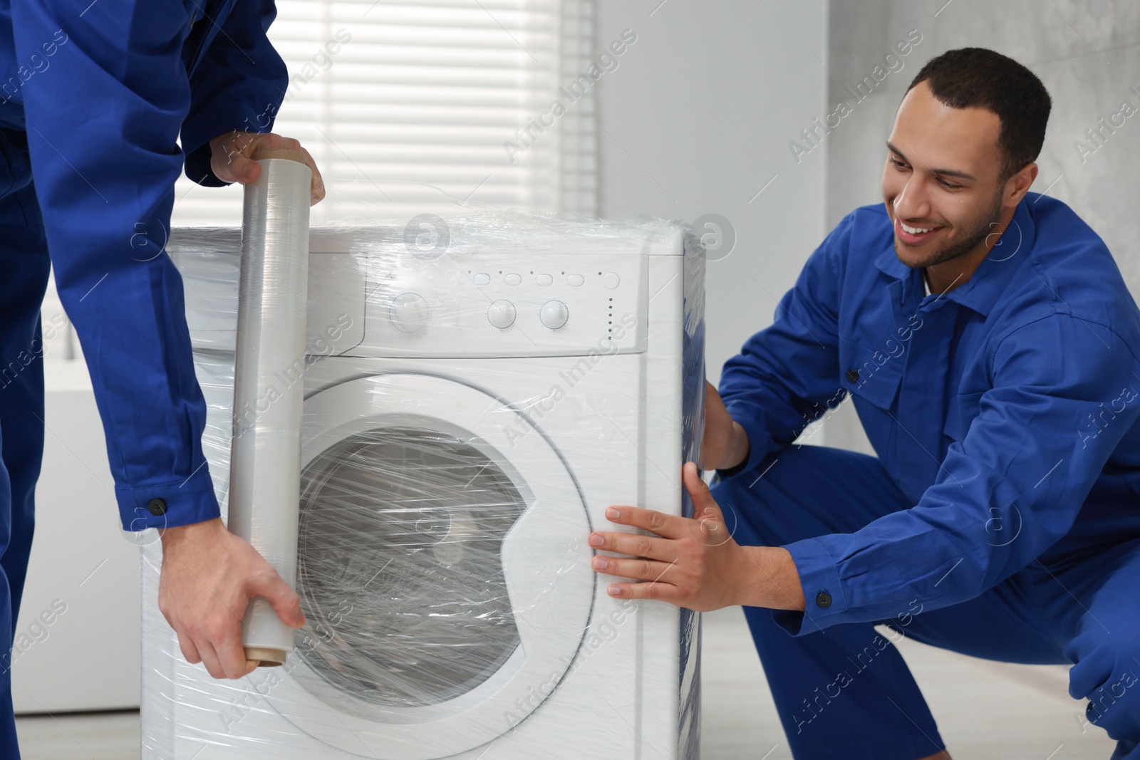 Photo of Male movers with stretch film wrapping washing machine in bathroom. New house