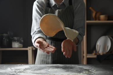 Photo of Woman tossing pizza dough at table in kitchen, closeup