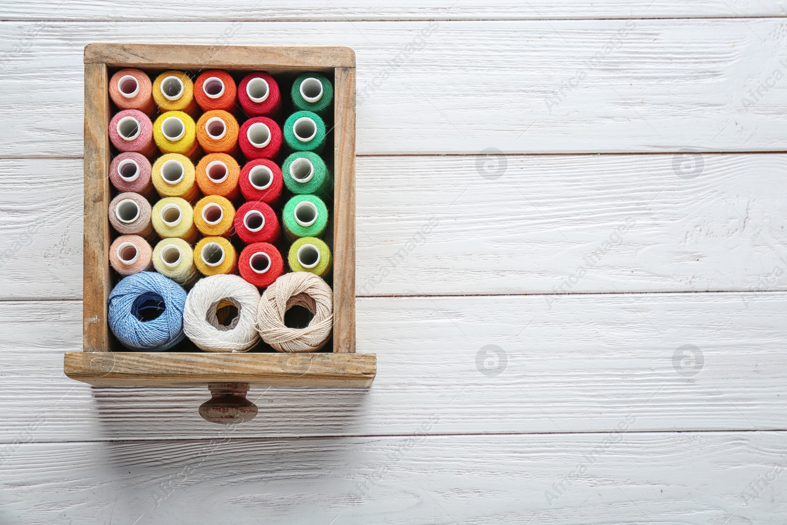 Photo of Drawer with colorful sewing threads on wooden background, top view