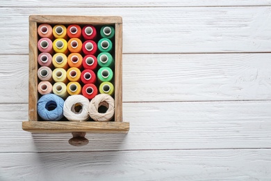 Drawer with colorful sewing threads on wooden background, top view