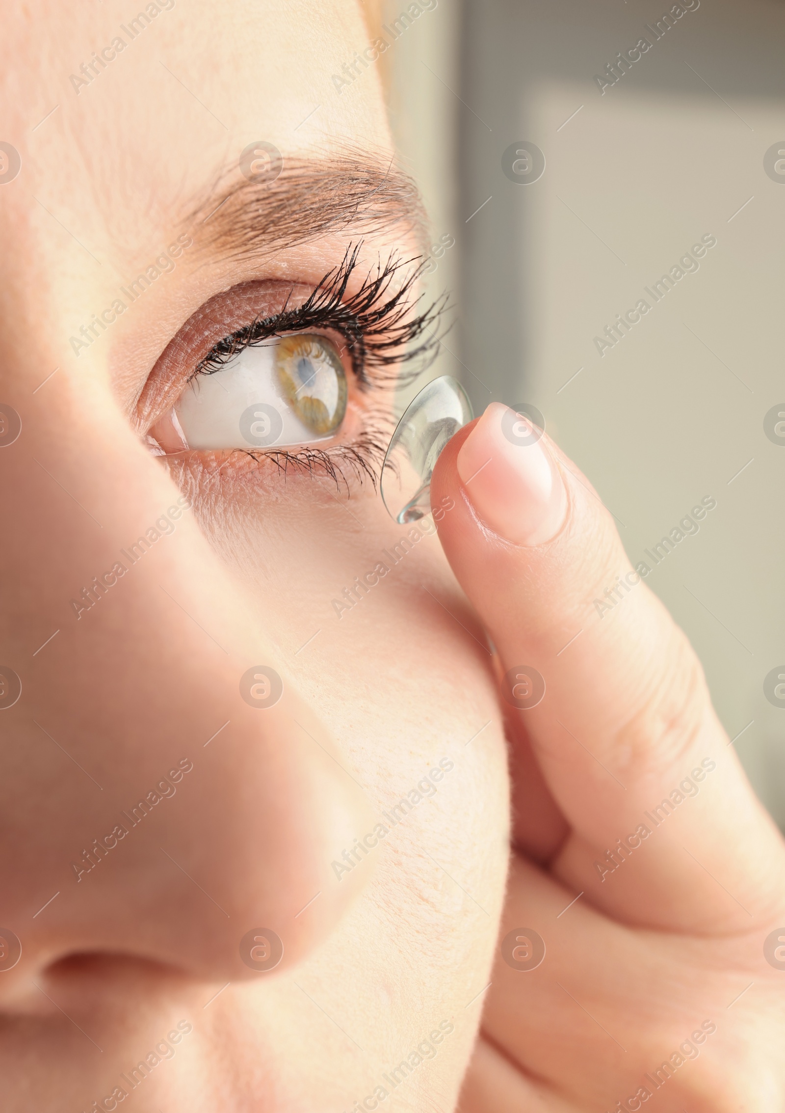 Photo of Young woman putting contact lens in her eye, closeup