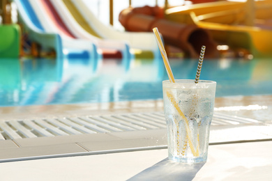 Glass of refreshing drink near swimming pool. Space for text