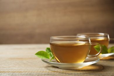 Photo of Cups of green tea and leaves on wooden table. Space for text