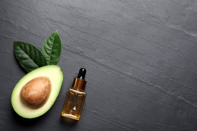 Photo of Bottle of essential oil, green leaves and fresh avocado on black table, flat lay. Space for text