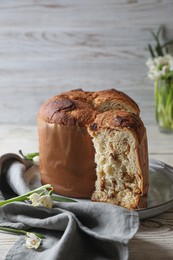 Photo of Delicious cut Panettone cake and beautiful flowers on light wooden table. Traditional Italian pastry
