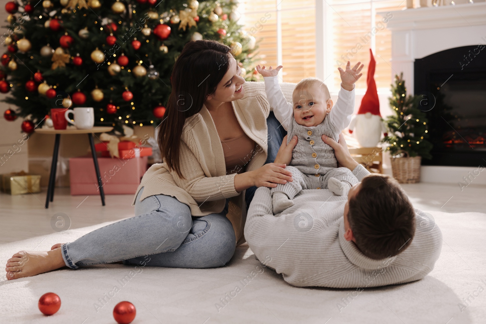 Photo of Happy family with cute baby on floor in room decorated for Christmas