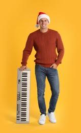 Photo of Man in Santa hat with synthesizer on yellow background. Christmas music