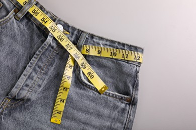 Jeans with measuring tape on light grey background, top view. Weight loss concept