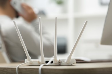 Photo of Man talking on smartphone while working at wooden table indoors, focus on Wi-Fi router