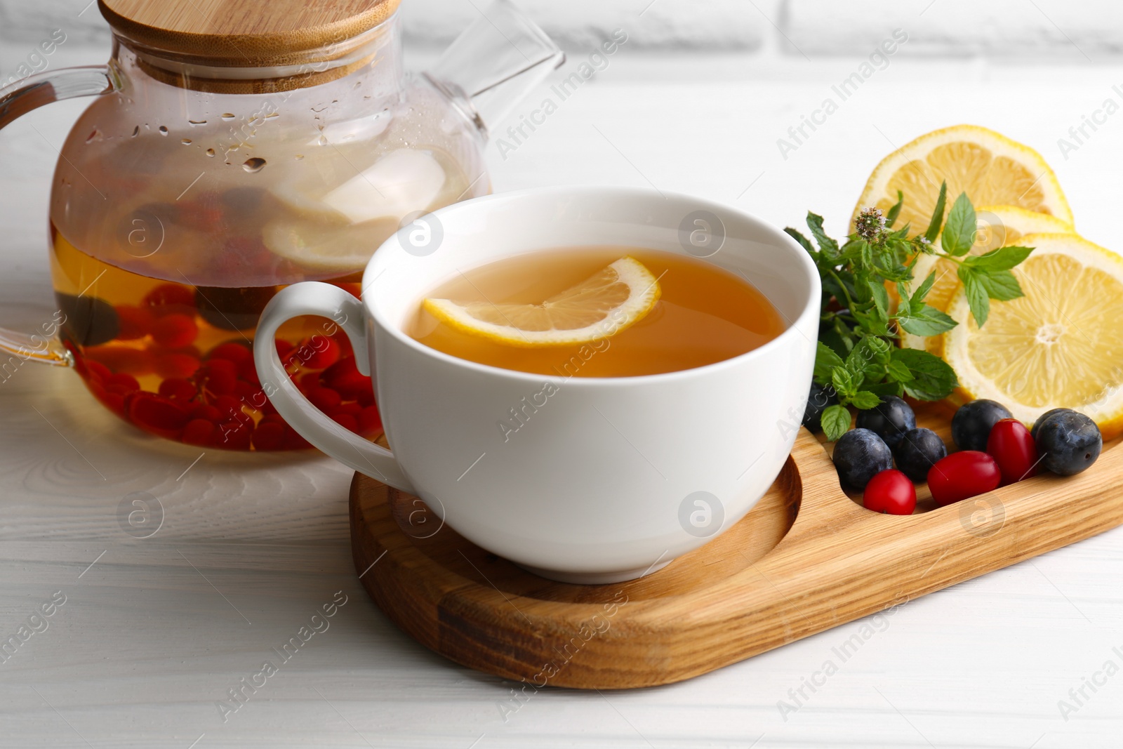 Photo of Cup with delicious immunity boosting tea and ingredients on white wooden table, closeup