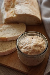 Photo of Sourdough starter in glass jar and bread on table