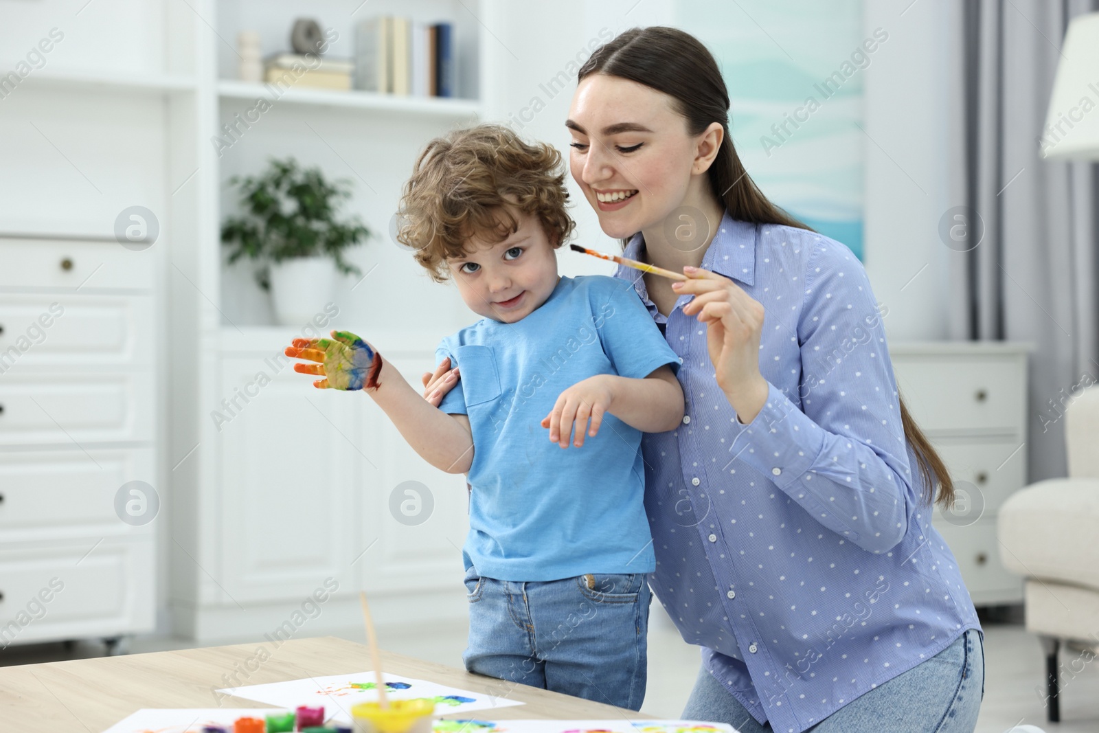 Photo of Mother and her little son painting with palms at home