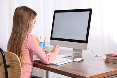 E-learning. Cute girl taking notes during online lesson at table indoors