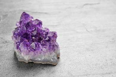 Beautiful purple amethyst gemstone on grey table, space for text