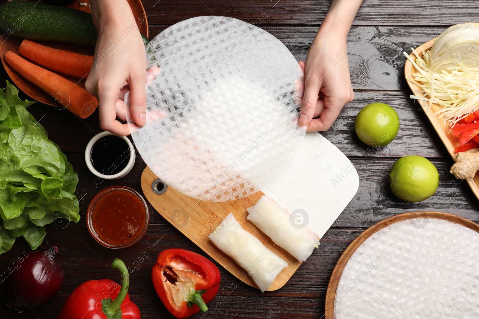 Photo of Making delicious spring rolls. Woman with fresh rice paper at wooden table, flat lay