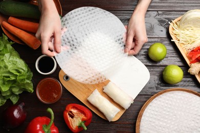 Photo of Making delicious spring rolls. Woman with fresh rice paper at wooden table, flat lay