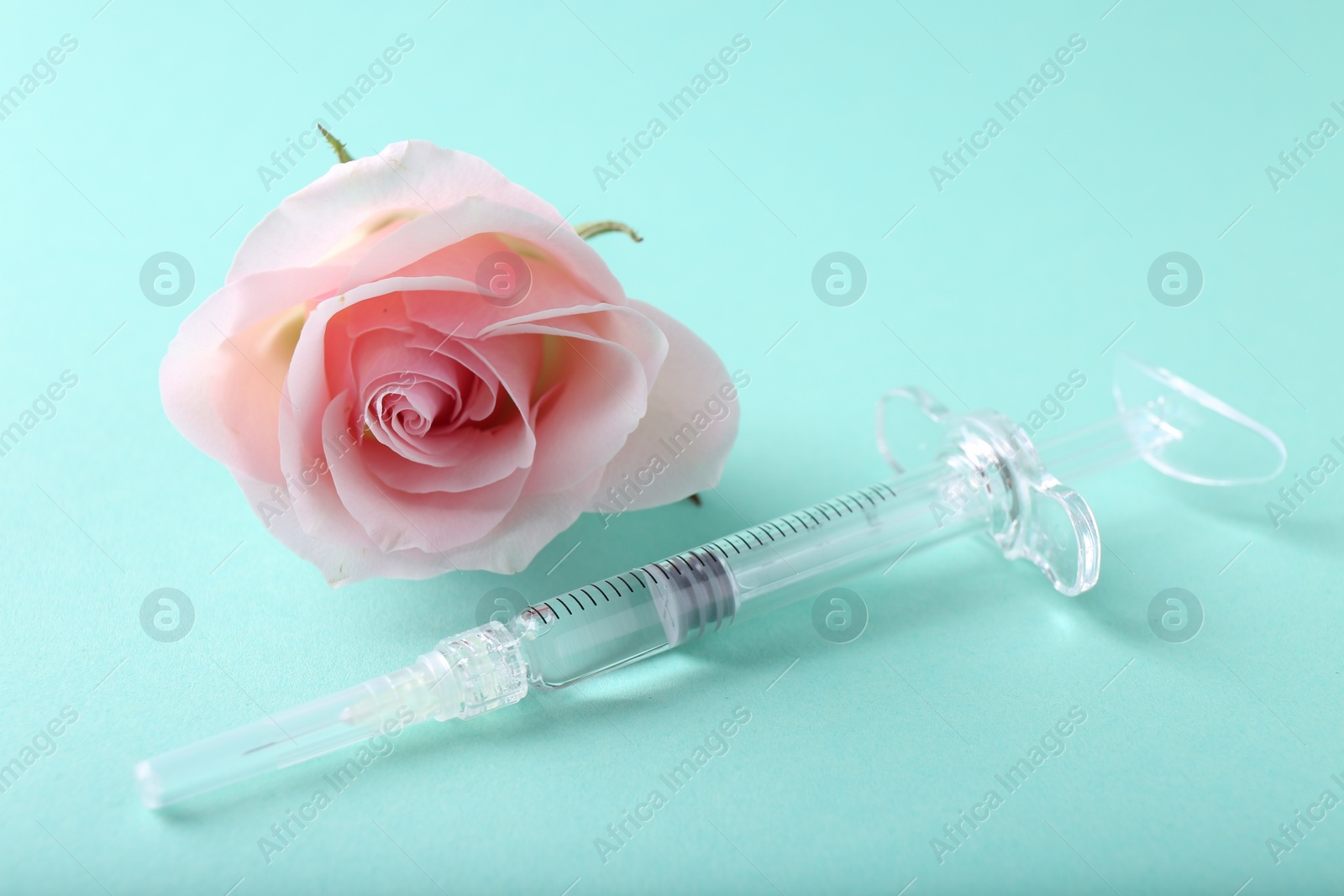 Photo of Cosmetology. Medical syringe and rose flower on turquoise background, closeup