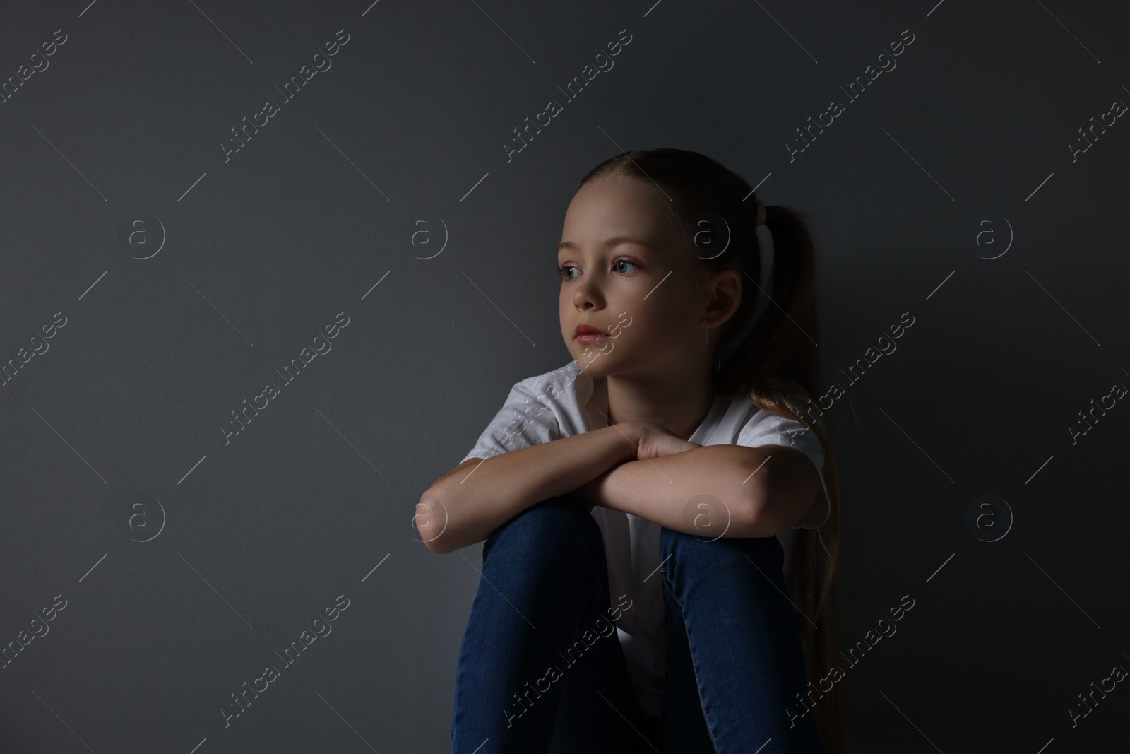 Photo of Sad girl sitting near dark grey background, space for text