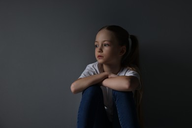 Sad girl sitting near dark grey background, space for text