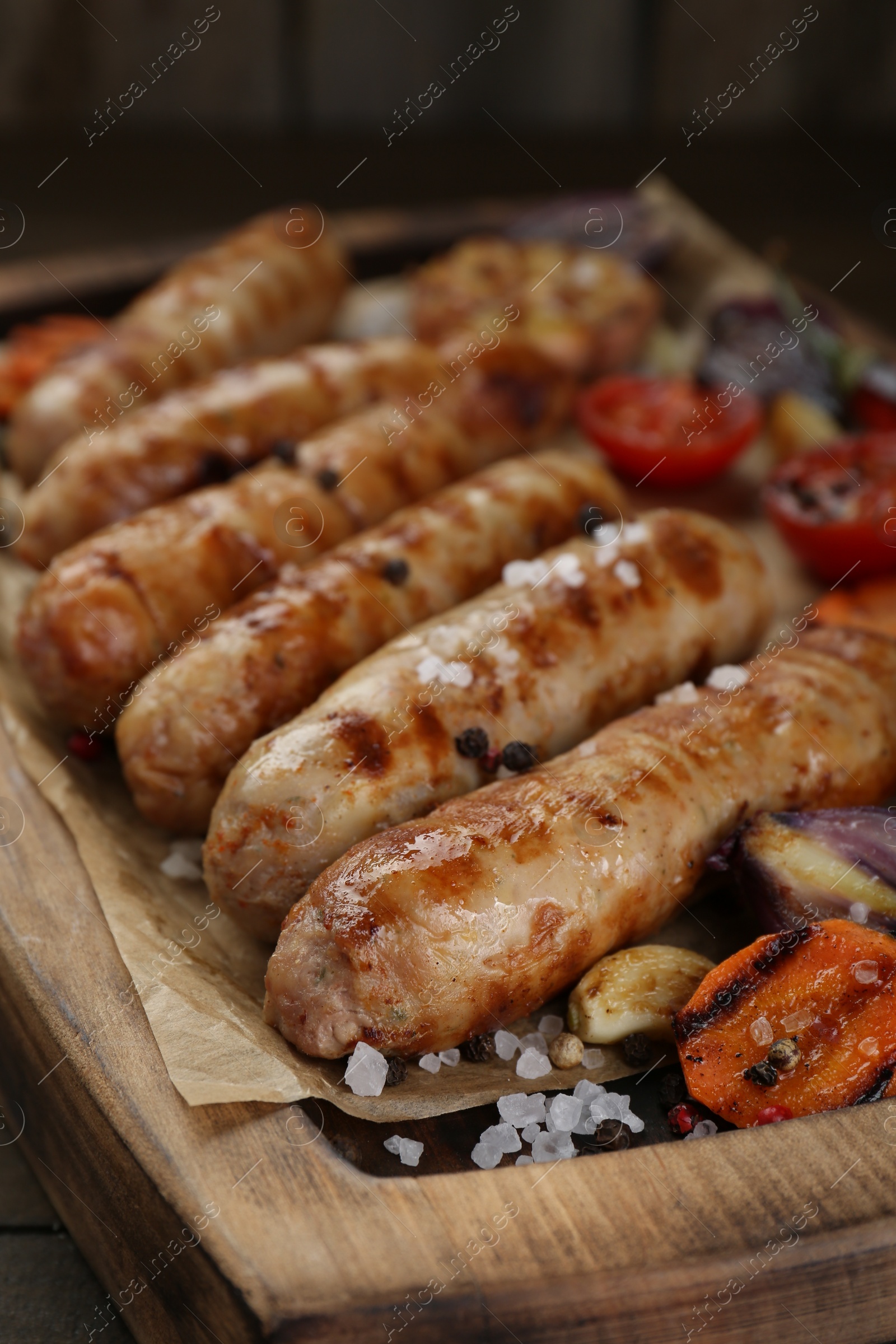 Photo of Tasty grilled sausages with vegetables on wooden table, closeup