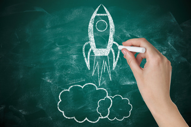 Image of Business startup concept. Woman drawing rocket on chalkboard, closeup