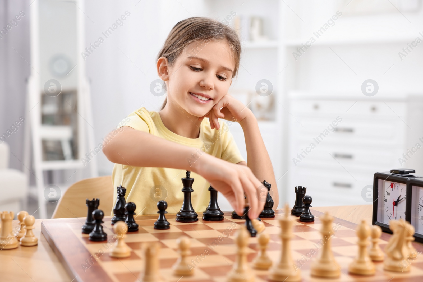Photo of Cute girl playing chess at table in room