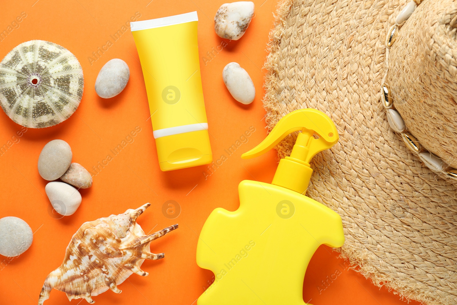 Photo of Suntan products, straw hat and seashells on orange background, flat lay