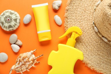 Photo of Suntan products, straw hat and seashells on orange background, flat lay