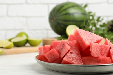 Photo of Slices of delicious watermelon and limes on white wooden table, closeup. Space for text