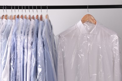 Hangers with shirts in dry cleaning plastic bags on rack against light background