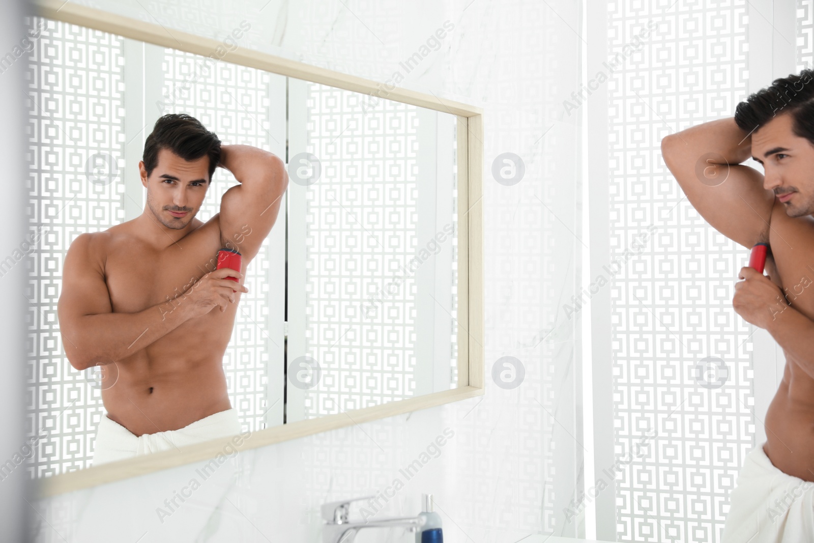 Photo of Handsome young man applying deodorant in bathroom