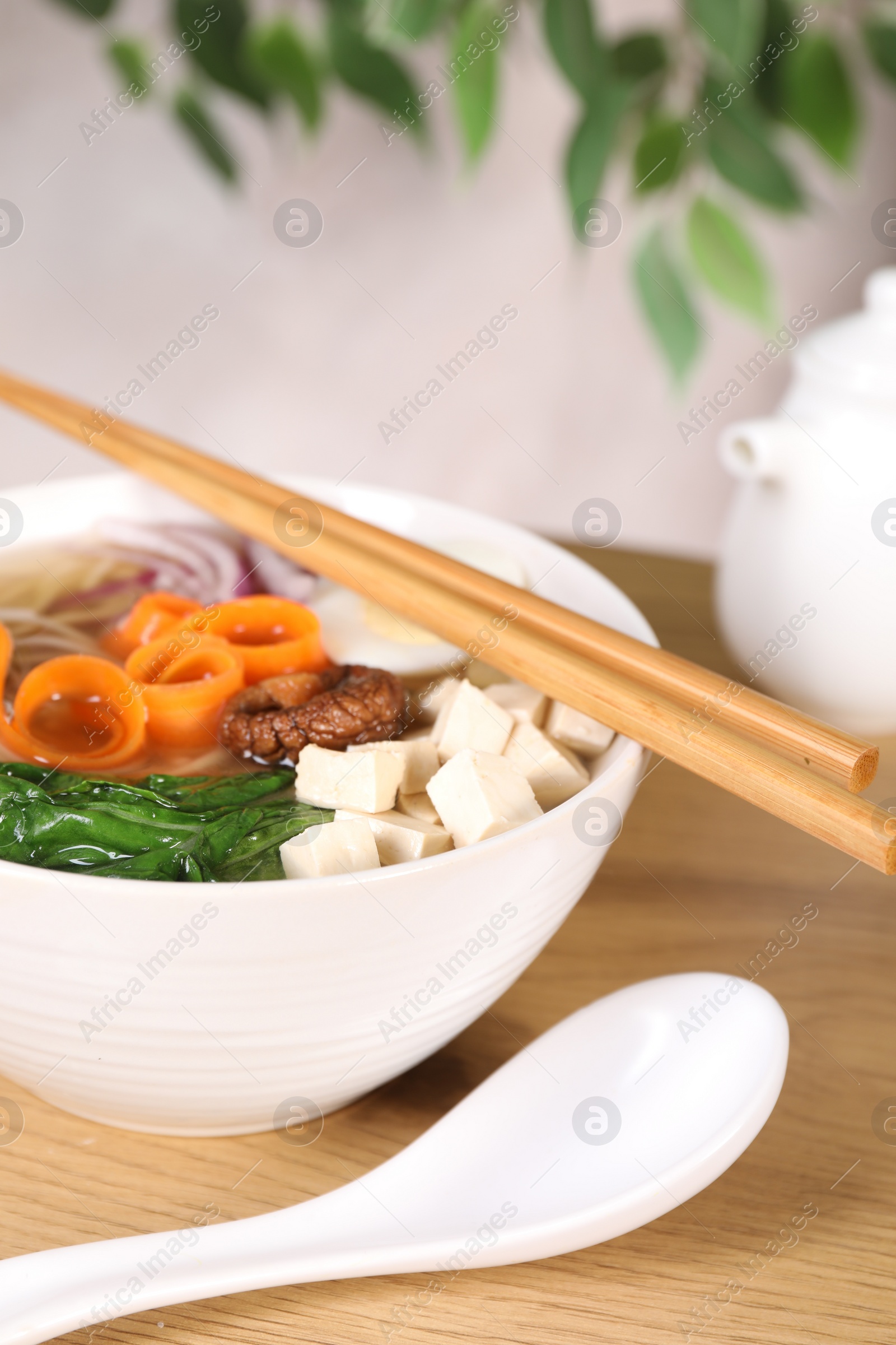 Photo of Delicious vegetarian ramen served on wooden table, closeup. Noodle soup