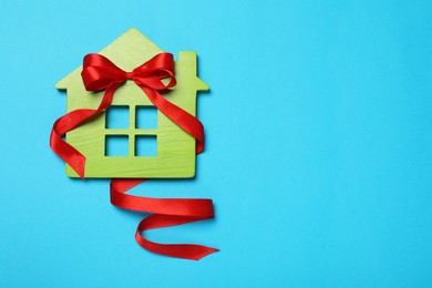 Photo of Wooden house model with red bow on light blue background, top view and space for text. Housewarming party