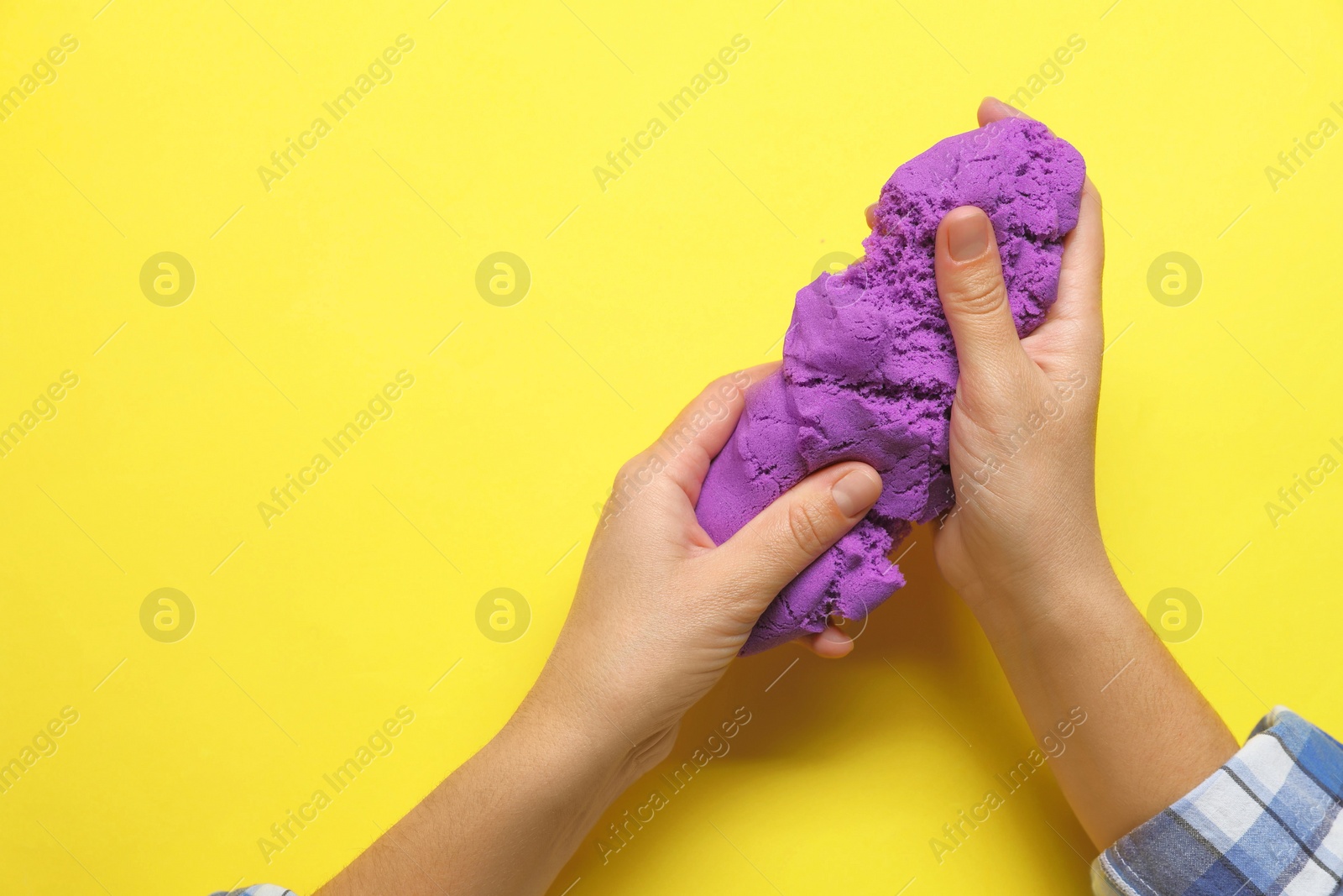 Photo of Woman playing with kinetic sand on yellow background, top view. Space for text