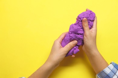 Photo of Woman playing with kinetic sand on yellow background, top view. Space for text