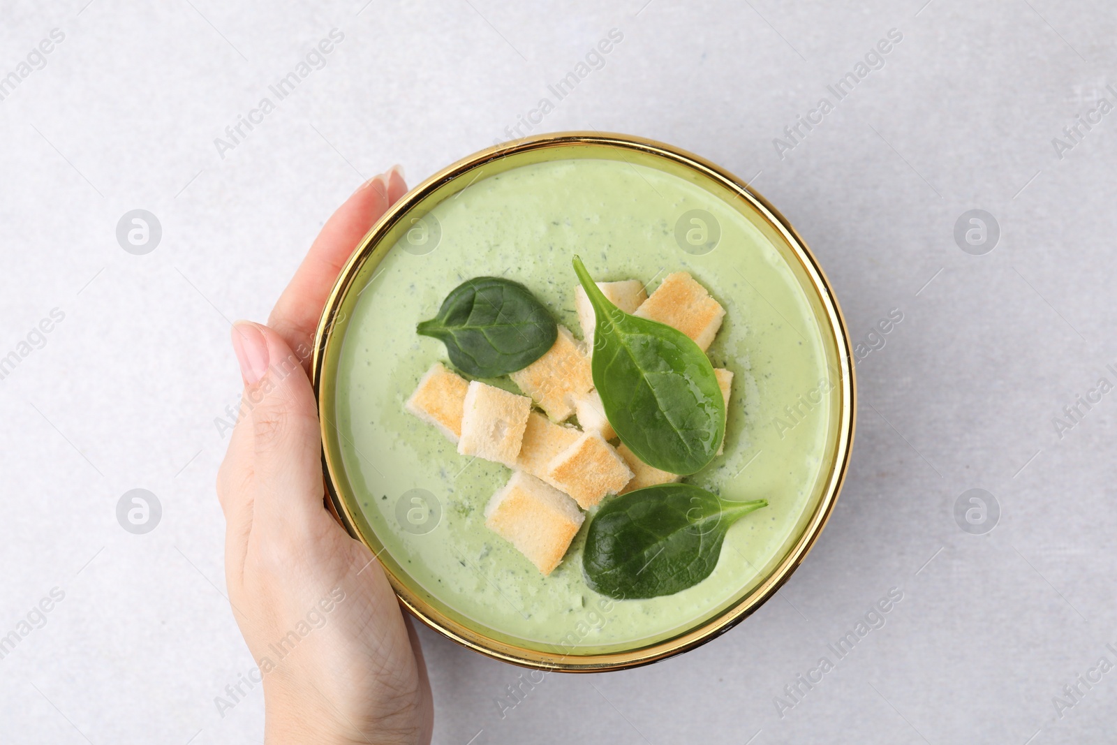 Photo of Woman with bowl of delicious spinach cream soup on light grey table, top view