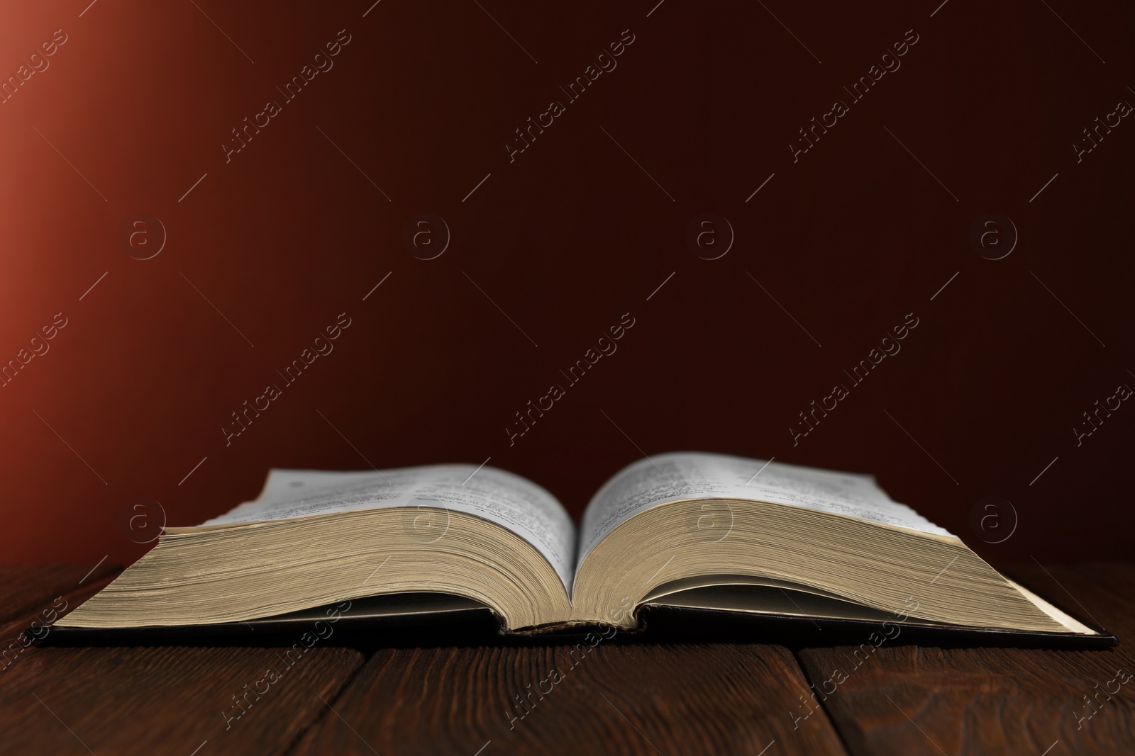 Photo of Open Bible on wooden table against brown background. Space for text