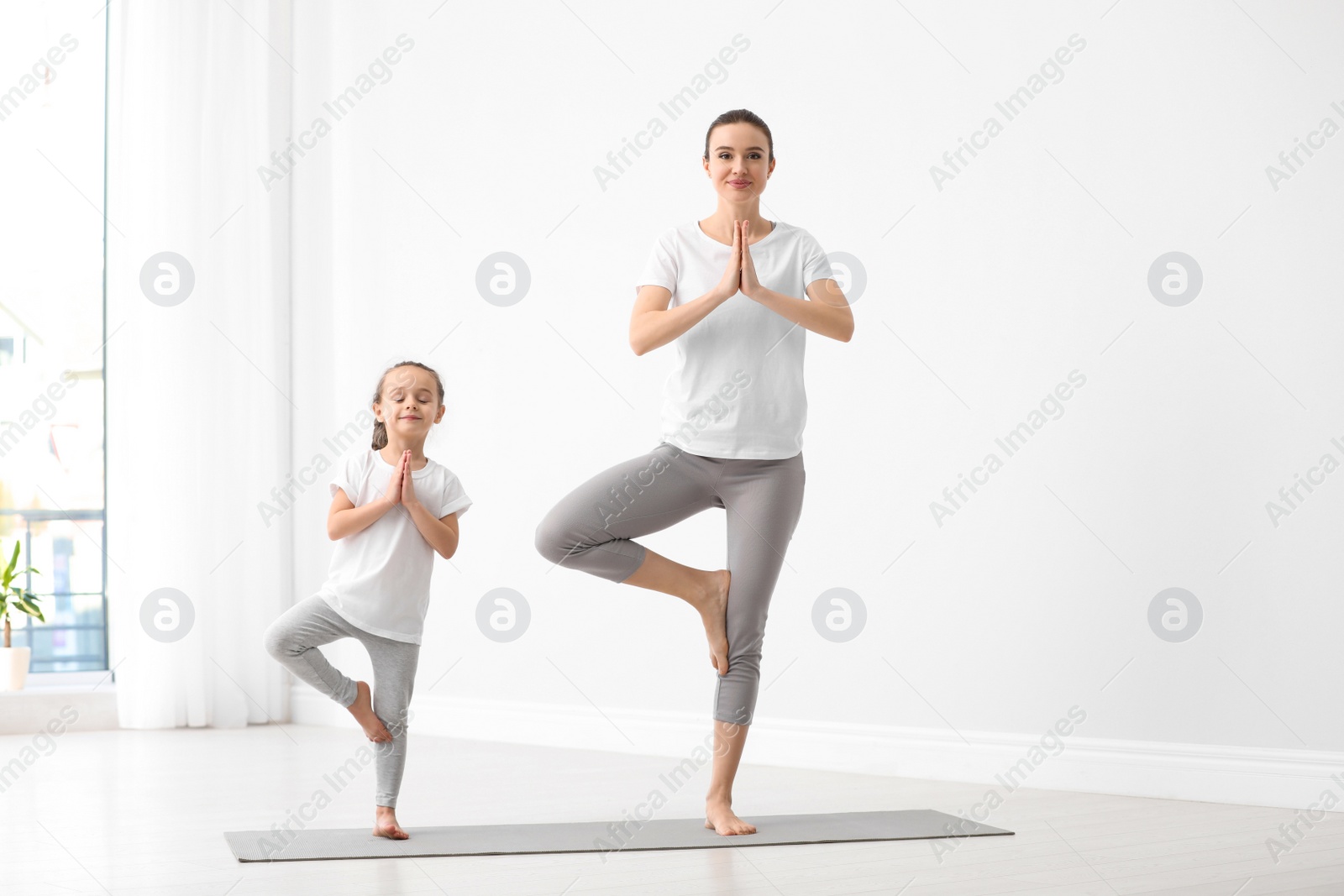 Photo of Young mother with little daughter practicing yoga at home