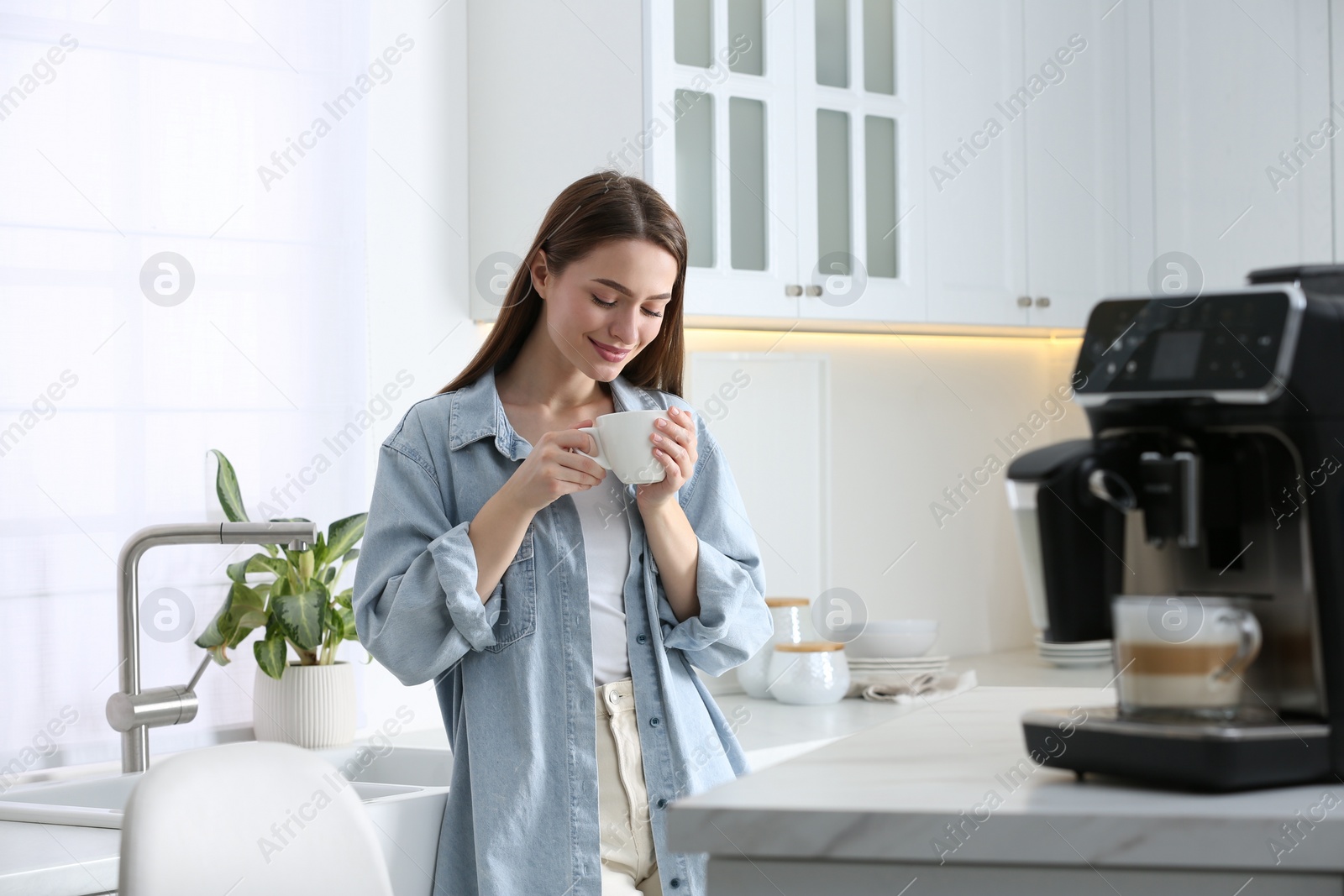 Photo of Young woman enjoying fresh aromatic coffee near modern machine in kitchen