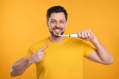 Photo of Happy man holding electric toothbrush on yellow background