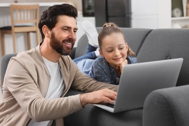 Photo of Happy man and his daughter with laptop on sofa at home