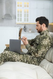 Photo of Soldier with laptop using smartphone at home. Military service